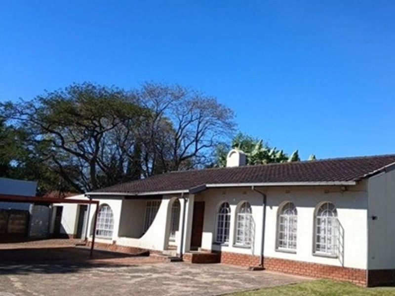 Front exterior view of a single-story residence featuring arched windows, a tiled roof, and an attached carport area with paved driveway.