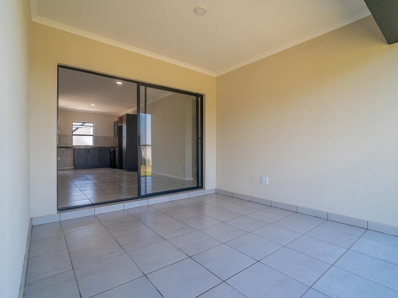 A clean, covered patio area featuring tiled flooring and a large sliding glass door providing access to the interior living space.
