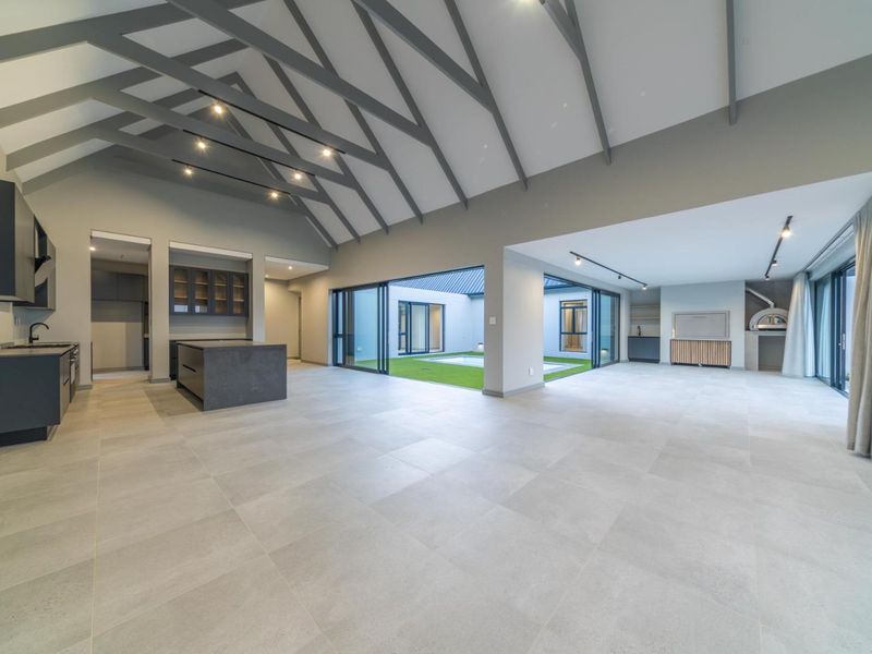 Spacious open-plan living and kitchen area featuring a vaulted ceiling with exposed rafters, modern cabinetry, and seamless access to a central courtyard.