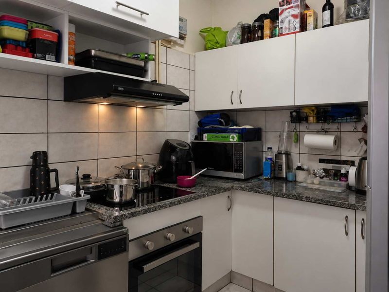 Compact kitchen featuring white cabinetry, granite countertops, ceramic tile backsplash, and built-in appliances including an oven, hob, and extractor fan.