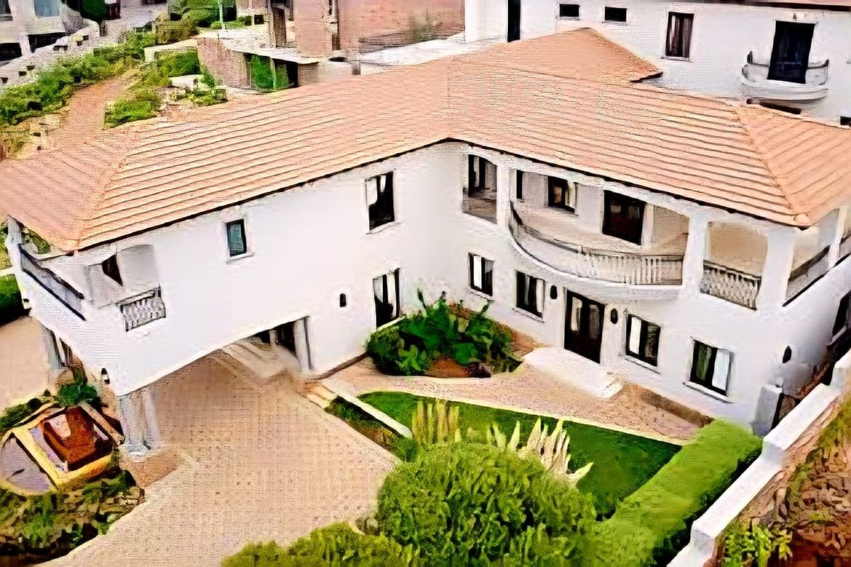An aerial view of a two-story residential property featuring a tiled roof, white exterior walls, a balcony, and a paved driveway.
