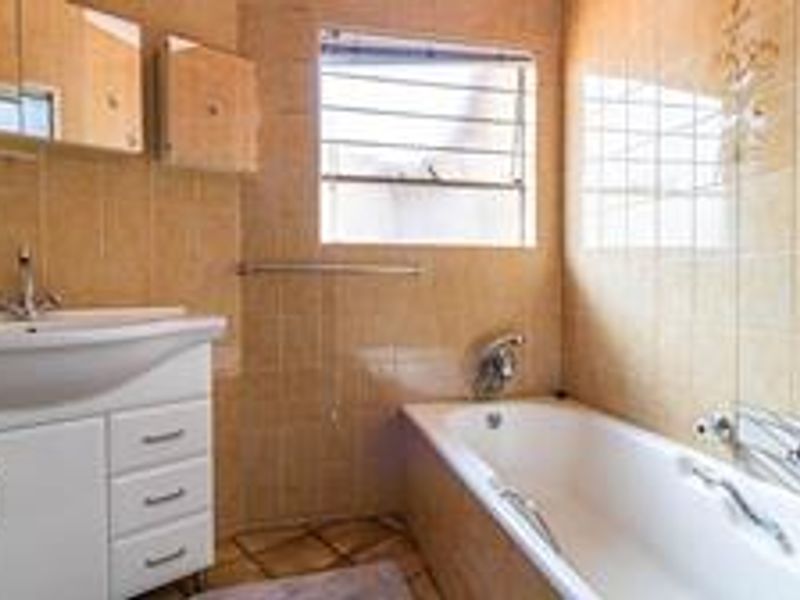 A functional bathroom featuring a white vanity with basin, a bathtub, and neutral wall tiling, providing a clean and practical space.