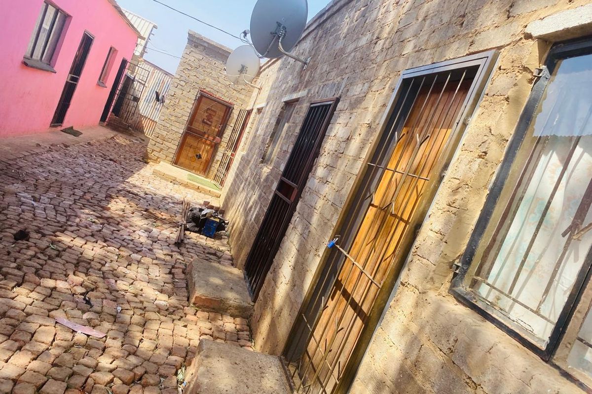A narrow exterior walkway featuring cobblestone paving, exposed brick walls, and multiple security-gated entrances.