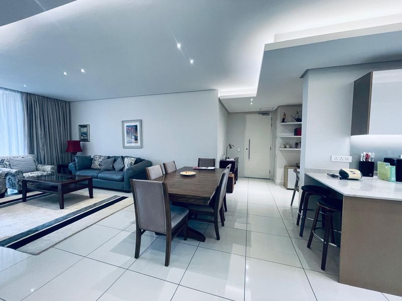 Modern open-plan living and dining area featuring sleek porcelain tiling, recessed cove lighting, and a contemporary kitchen with a stone breakfast bar.