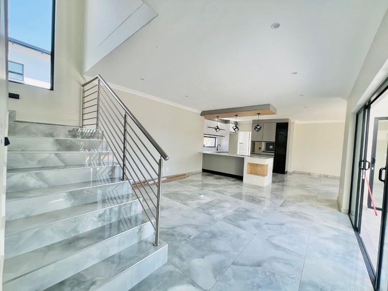 Spacious open-plan living area featuring high-end marble-look floor tiles, a modern kitchen with island, and a sleek staircase with stainless steel balustrades.