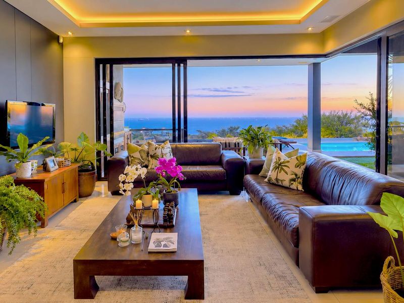 Spacious living room featuring recessed cove lighting, large sliding glass doors, and seamless indoor-outdoor flow with panoramic ocean views.