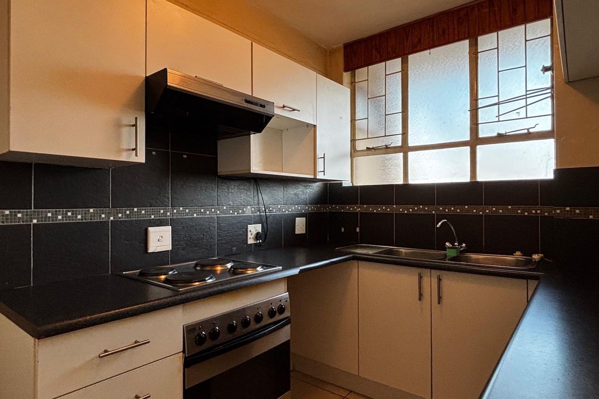 A functional kitchen featuring white cabinetry, dark countertops, a built-in oven with hob, extractor fan, and a stainless steel sink.