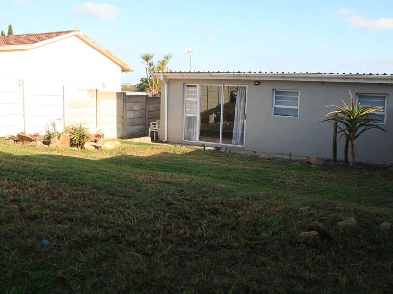 Rear view of the cottage featuring a lawn, concrete boundary walls, and sliding glass door access.