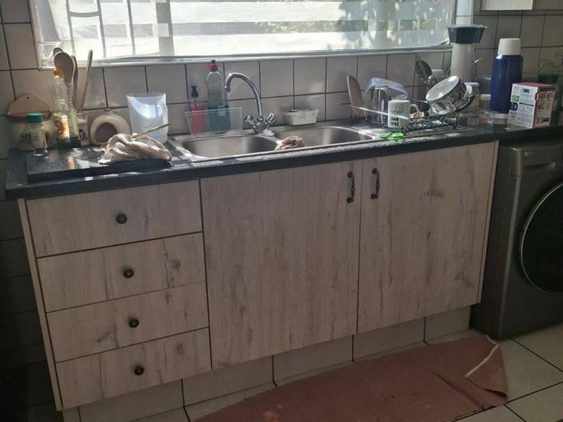 A functional kitchen area featuring light wood-finish cabinetry, a double basin sink, tiled backsplash, and space for an integrated washing machine.