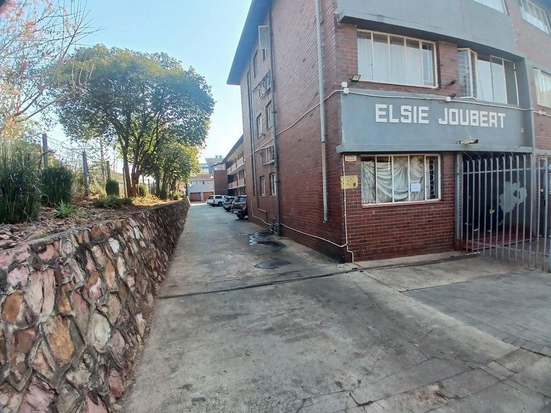 Exterior view of the Elsie Joubert apartment building, featuring a brick facade, stone retaining wall, and concrete driveway access.