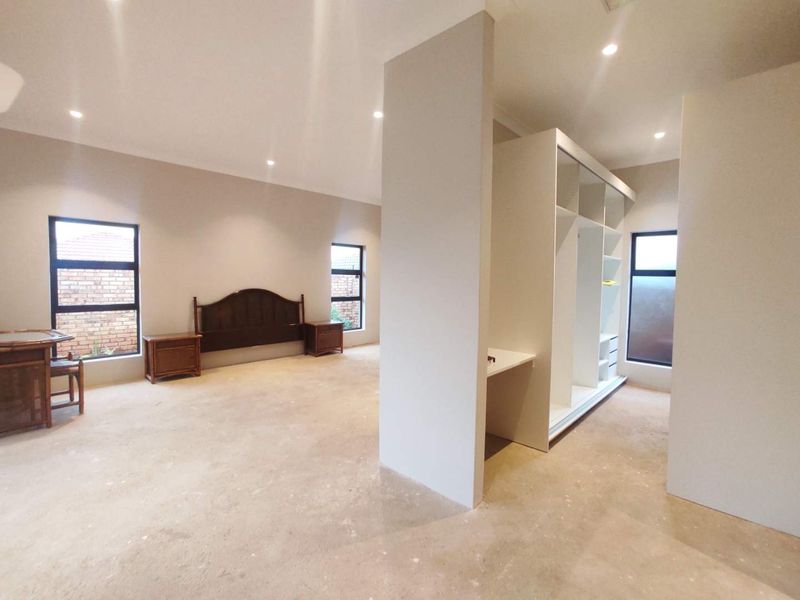 Spacious bedroom featuring a built-in wardrobe, recessed lighting, and large windows, currently awaiting final flooring installation.