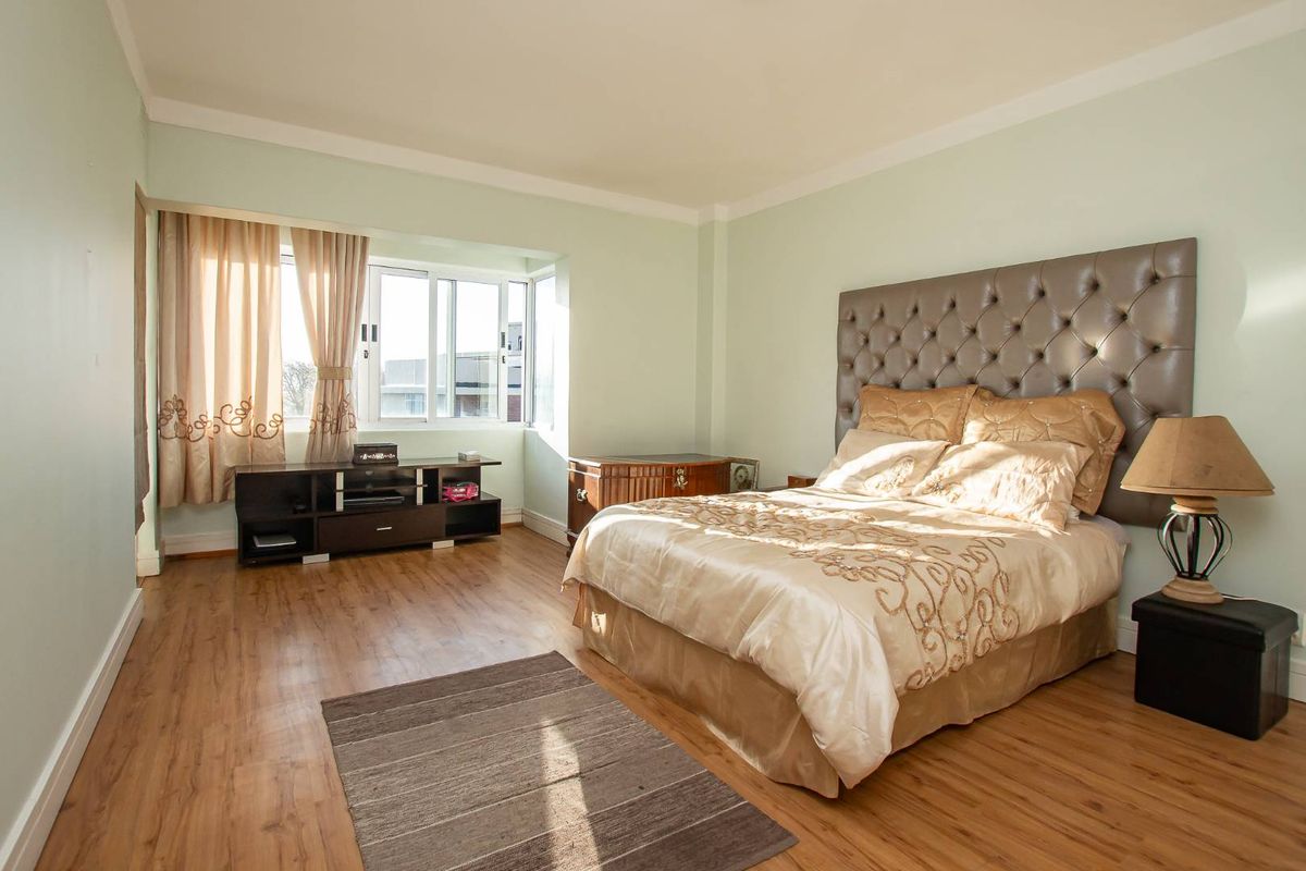 A spacious bedroom featuring light green walls, laminate wood flooring, and a large window that allows for ample natural light.