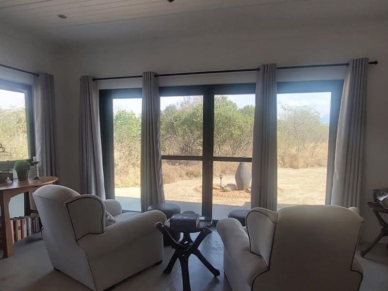 A bright living area featuring concrete floors, a modern ceiling fan, and large glass doors providing natural light and views of the surrounding landscape.