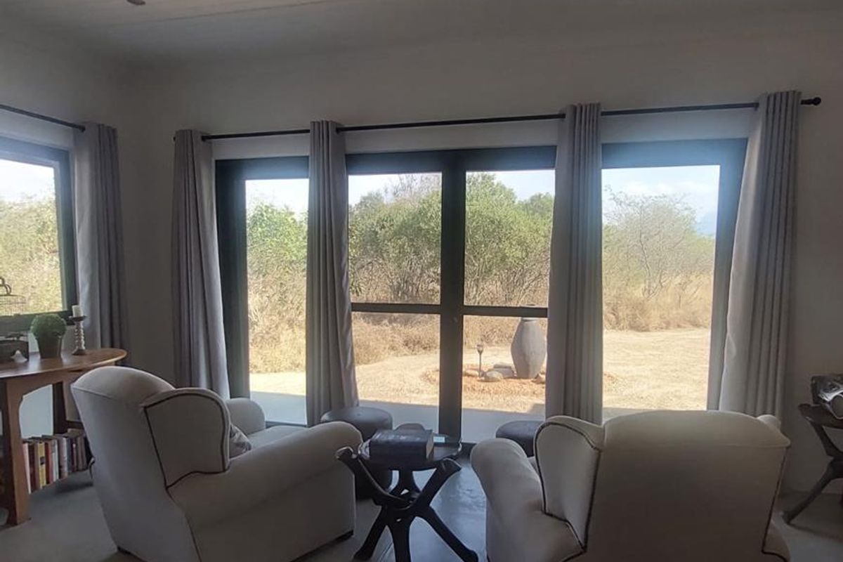 A bright living area featuring concrete floors, a modern ceiling fan, and large glass doors providing natural light and views of the surrounding landscape.