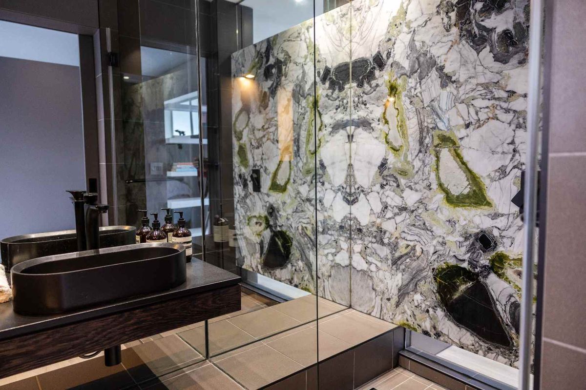Modern bathroom featuring a striking marble feature wall, glass-enclosed shower, and a sleek dark vessel sink on a floating vanity.