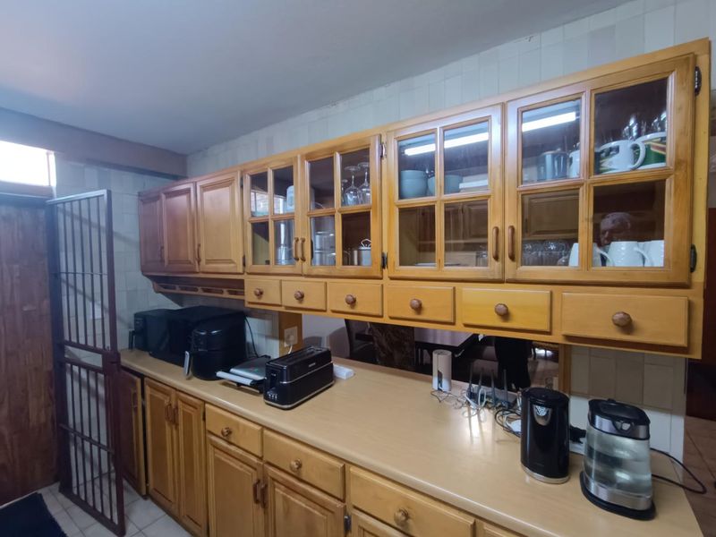 A functional kitchen featuring traditional wooden cabinetry with glass-fronted upper units, laminate countertops, and a tiled backsplash.