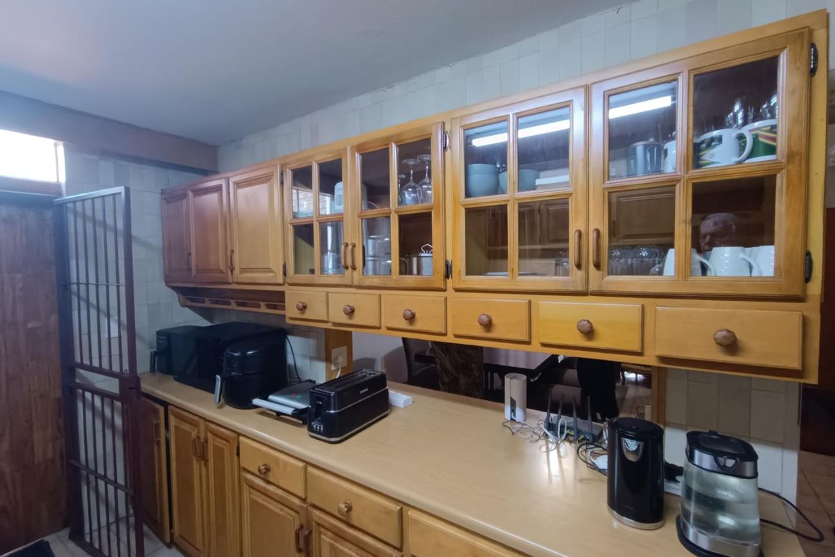 A functional kitchen featuring traditional wooden cabinetry with glass-fronted upper units, laminate countertops, and a tiled backsplash.
