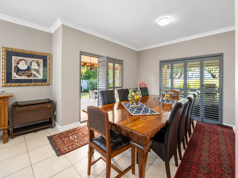 A well-maintained dining room featuring neutral walls, crown molding, tiled flooring, and plantation shutters with direct access to the outdoor patio area.