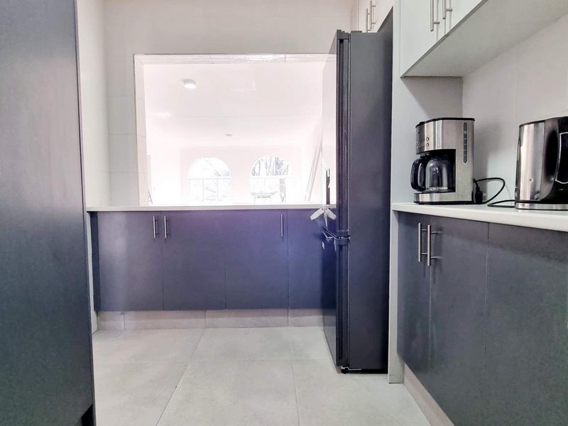 A modern kitchen featuring dark cabinetry, light countertops, and a convenient pass-through window looking into the adjacent living area.