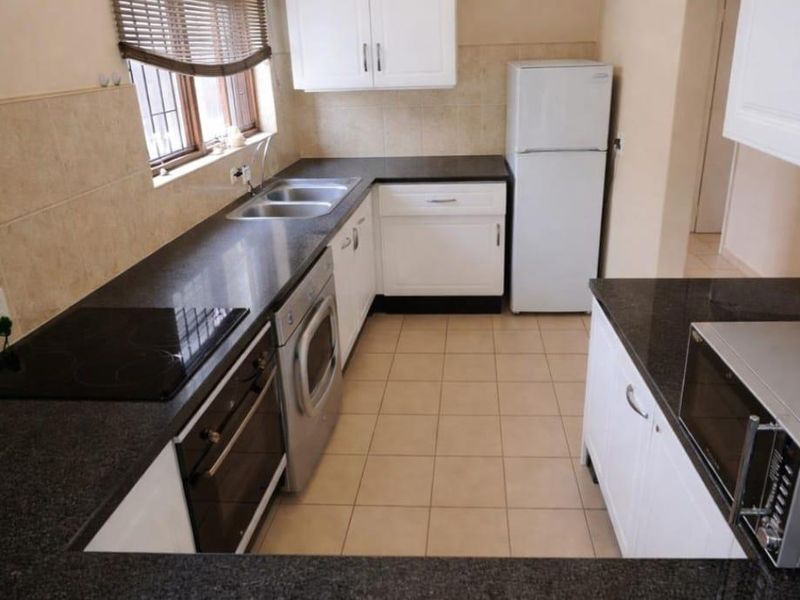 A functional kitchen featuring white cabinetry, dark granite countertops, a built-in oven and hob, and tiled finishes throughout.