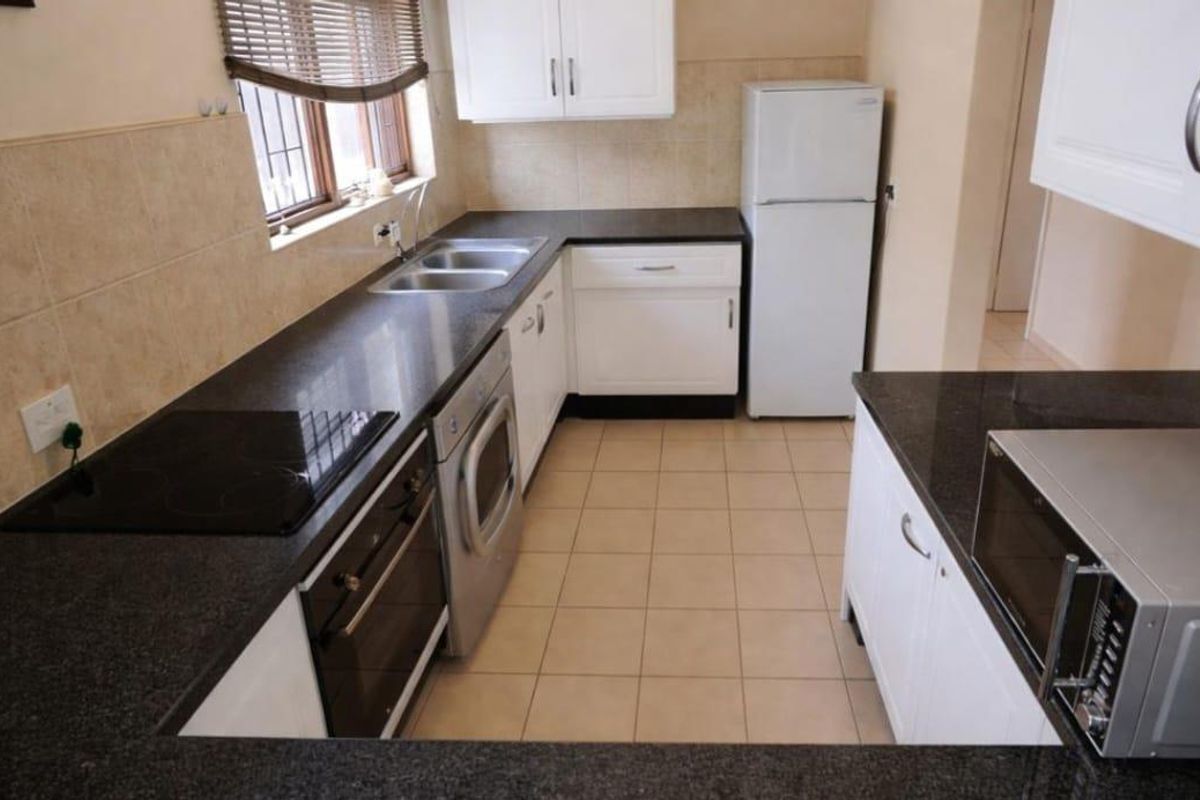 A functional kitchen featuring white cabinetry, dark granite countertops, a built-in oven and hob, and tiled finishes throughout.