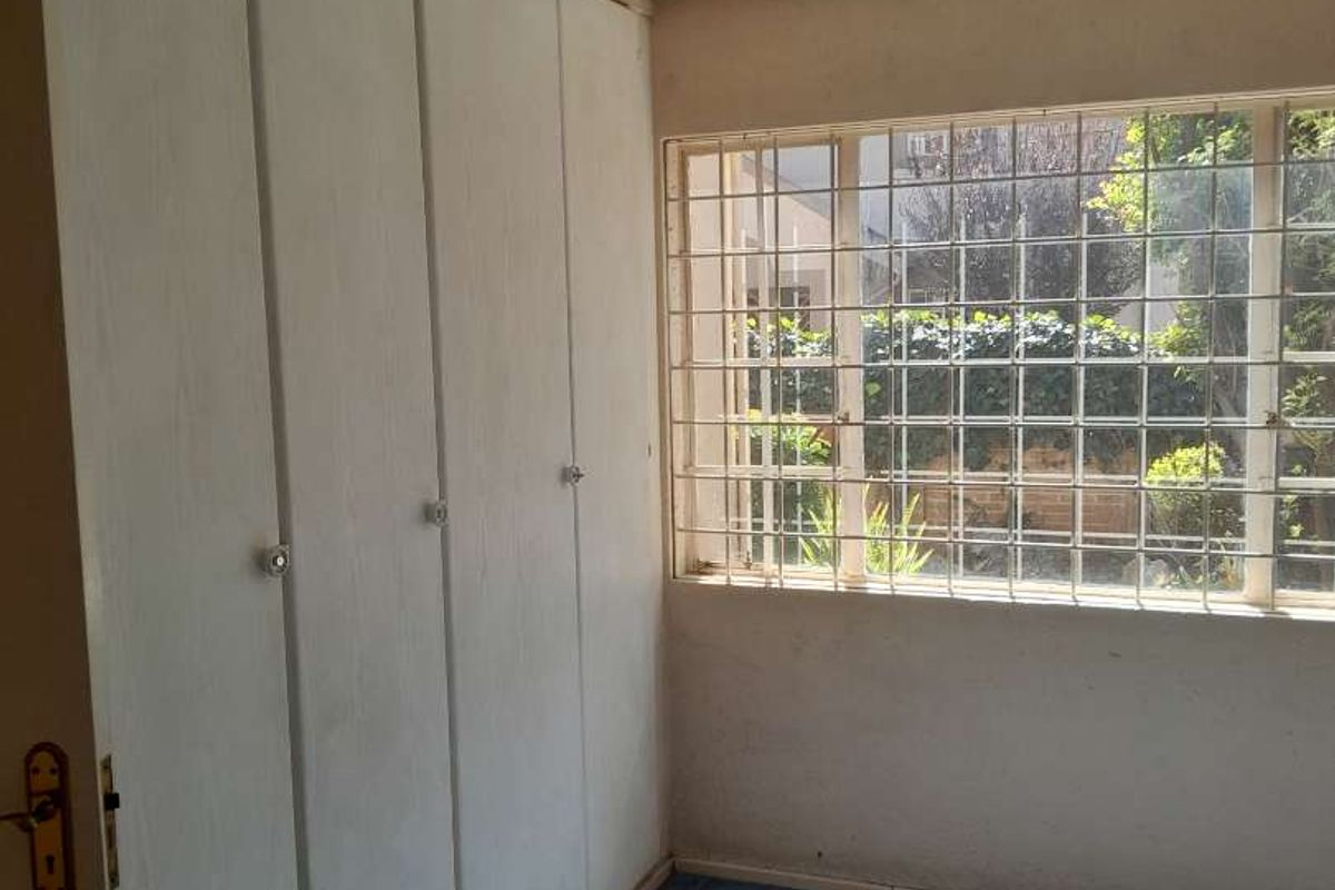 A bedroom featuring built-in cupboards, tiled flooring, and a window with security bars, offering a functional space with potential for modernization.