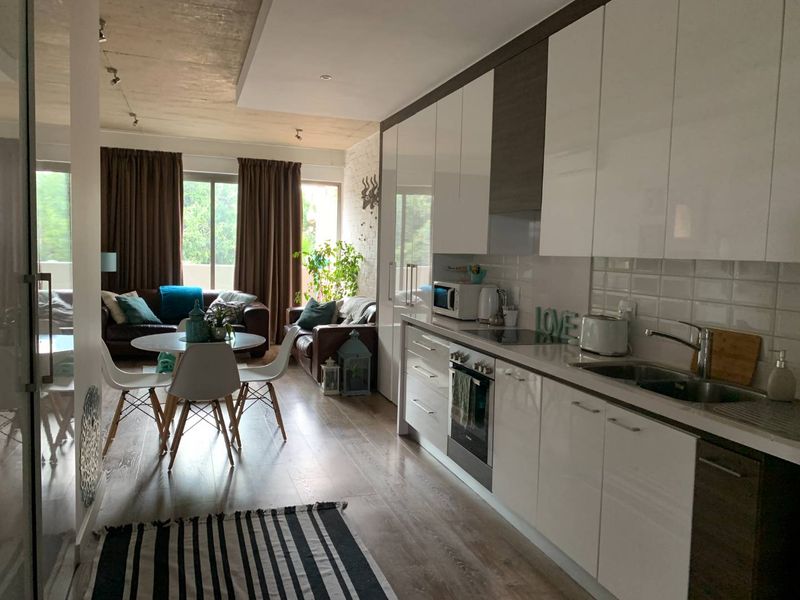 Modern open-plan living area featuring a sleek kitchen with high-gloss cabinetry, integrated appliances, and direct access to a balcony through sliding glass doors.