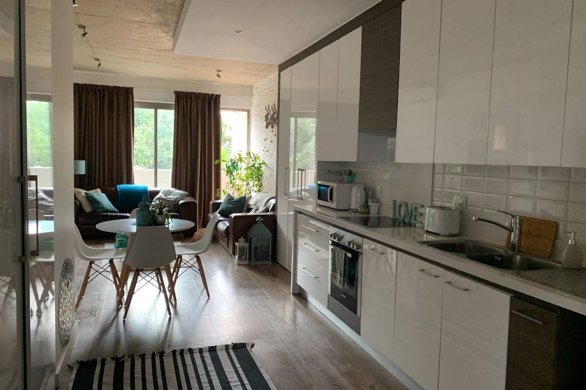 Modern open-plan living area featuring a sleek kitchen with high-gloss cabinetry, integrated appliances, and direct access to a balcony through sliding glass doors.