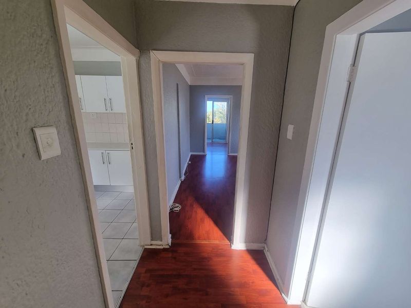 A bright hallway connecting to a kitchen and living area, featuring laminate and tiled flooring with neutral wall finishes.