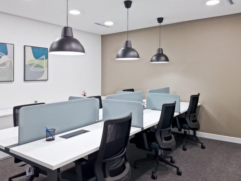 A modern, well-lit office space featuring built-in workstations with privacy screens, pendant lighting, and professional carpet flooring.