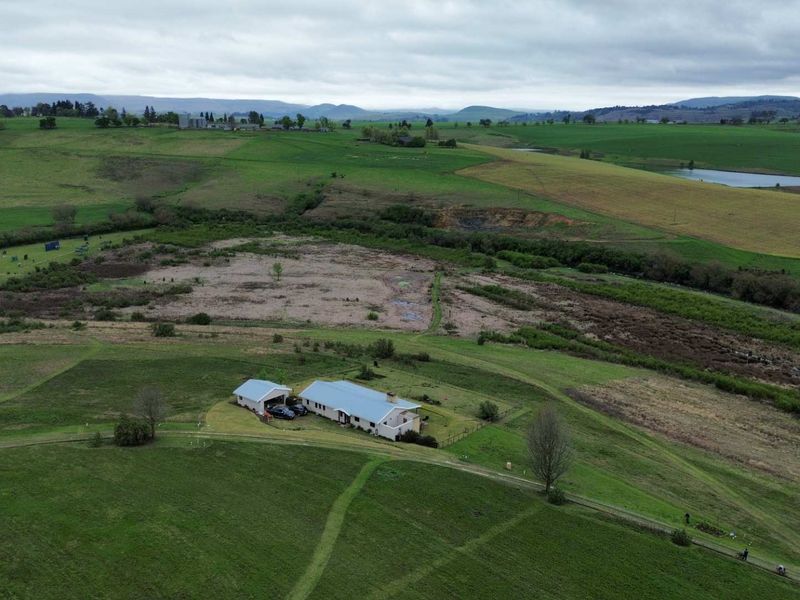 Aerial view of a residential property situated on a large, expansive rural plot with rolling green hills and natural landscape.