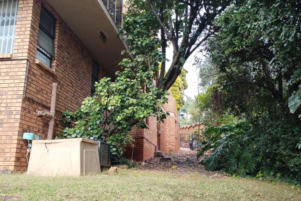 Rear view of the brick house featuring a lawn, mature landscaping, and an upper-level balcony with a glass balustrade.