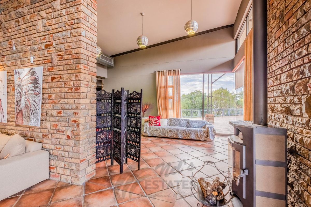 Spacious living area featuring a prominent exposed brick feature wall, terracotta floor tiles, a built-in fireplace, and large glass sliding doors leading to a patio.