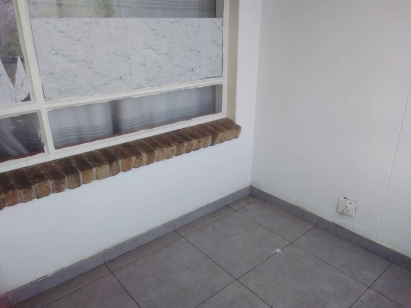 An empty interior space featuring grey tiled flooring, a brick window sill, and a neutral wall finish, suitable for various living area configurations.