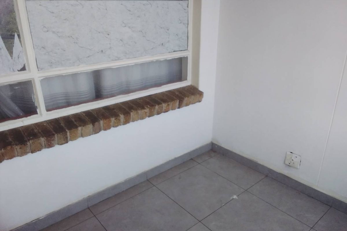 An empty interior space featuring grey tiled flooring, a brick window sill, and a neutral wall finish, suitable for various living area configurations.