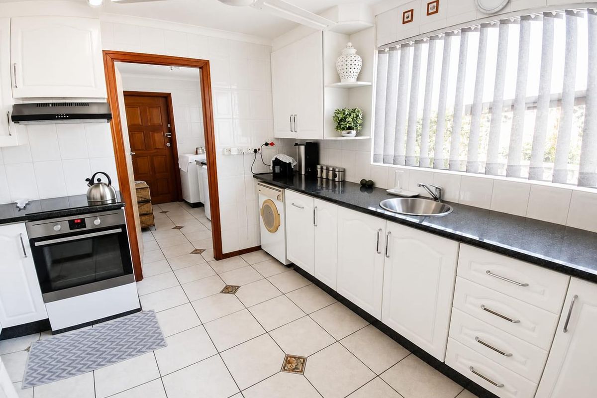 A functional kitchen featuring white cabinetry, dark granite countertops, a built-in oven, extractor fan, and a stainless steel sink with tiled flooring.