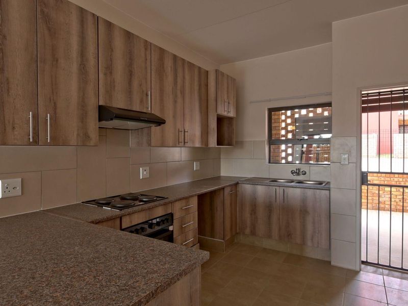 Modern kitchen featuring wood-look laminate cabinetry, granite countertops, built-in oven with hob, and a double bowl sink with direct access to an outdoor area.