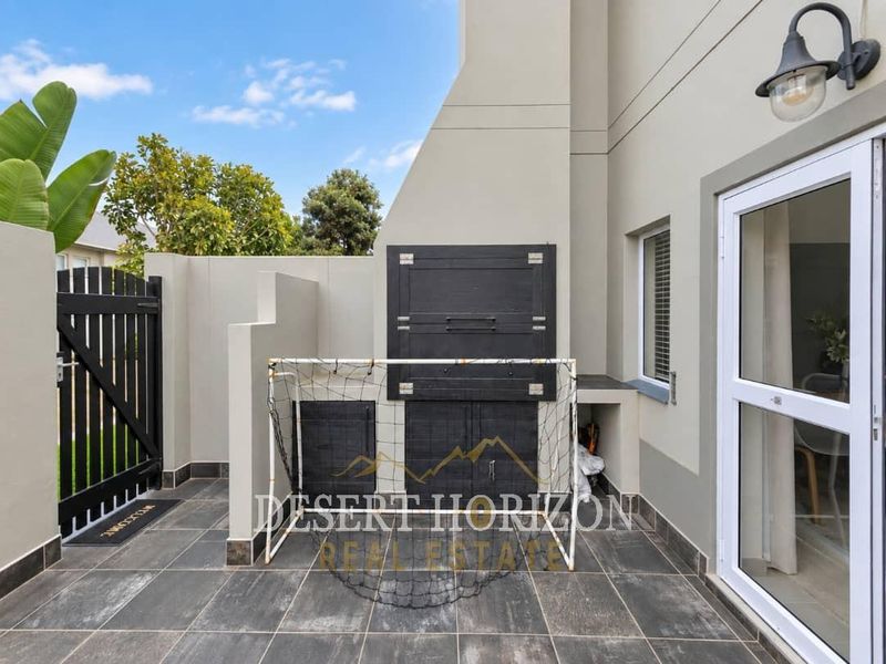 A neat, tiled patio area featuring a built-in braai, exterior lighting, and direct access to the home through a sliding door.