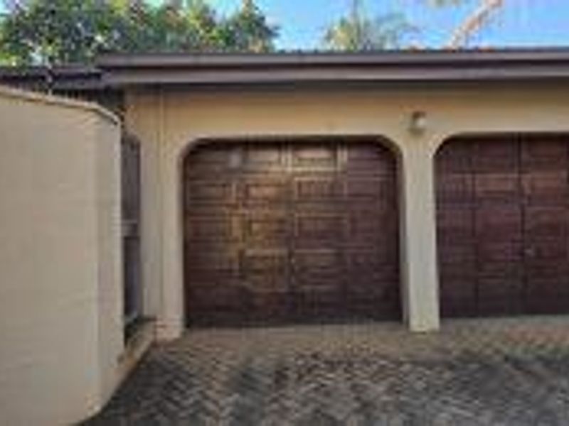 A double garage with wooden sectional doors and a paved driveway, featuring a curved exterior wall and integrated lighting.
