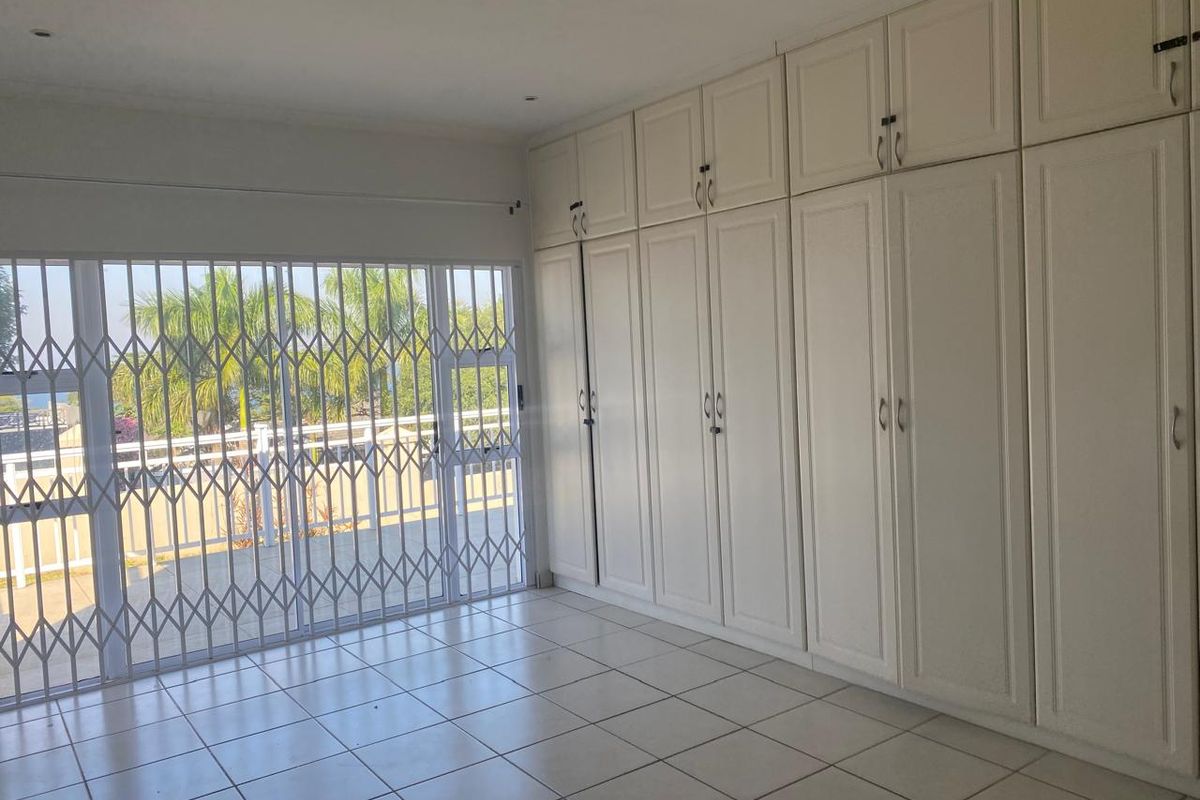 Spacious bedroom featuring extensive built-in cabinetry, tiled flooring, and large sliding doors with security gates leading to an outdoor area.