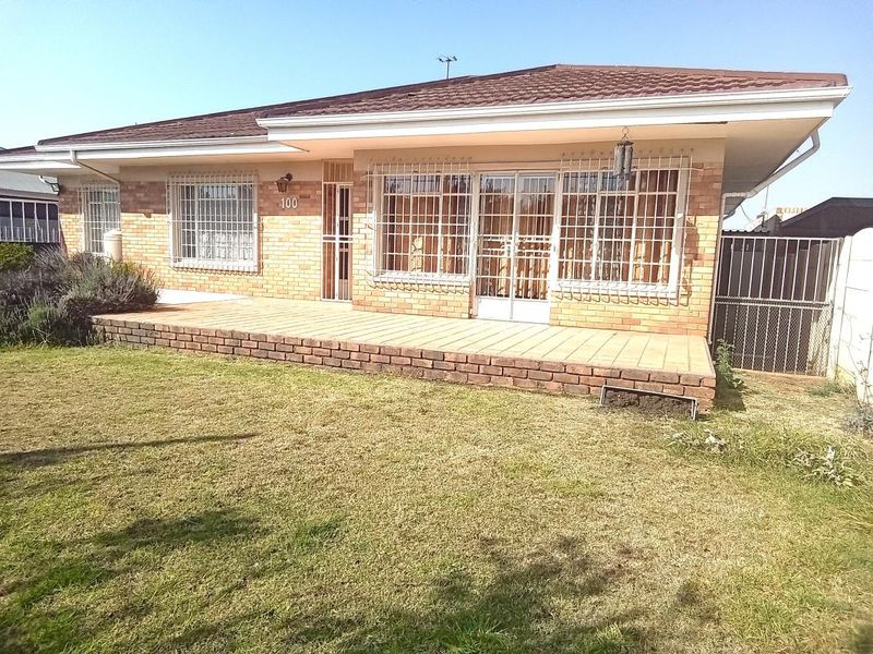 Rear view of a single-story brick house featuring a tiled patio, security bars on windows, and a spacious lawn area.