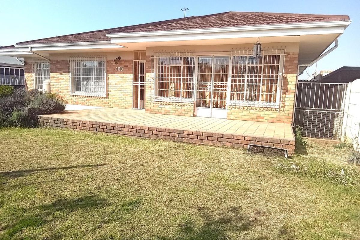 Rear view of a single-story brick house featuring a tiled patio, security bars on windows, and a spacious lawn area.