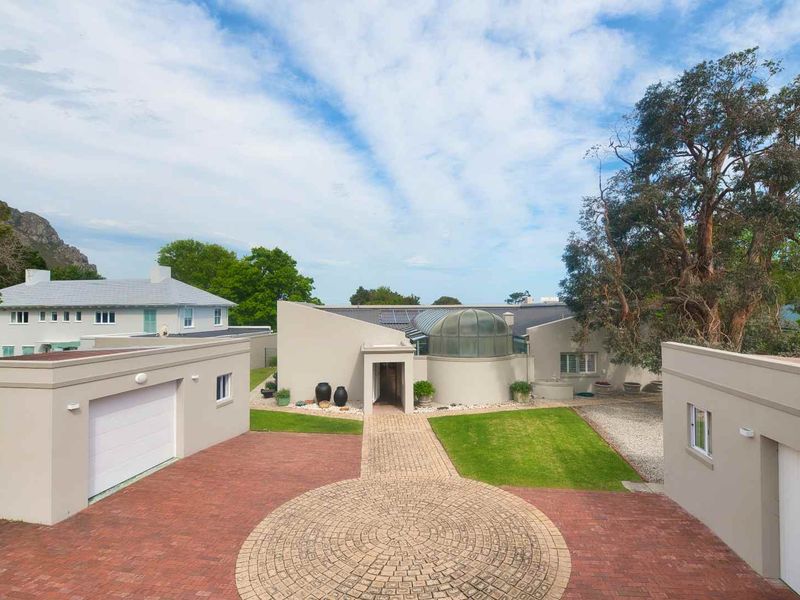A modern front elevation featuring a circular brick driveway, double garage, and a unique domed glass roof architectural element.