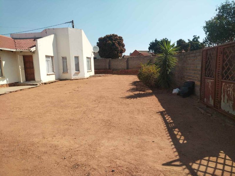 A spacious rear yard featuring a brick boundary wall, metal gate, and direct access to the main house structure.