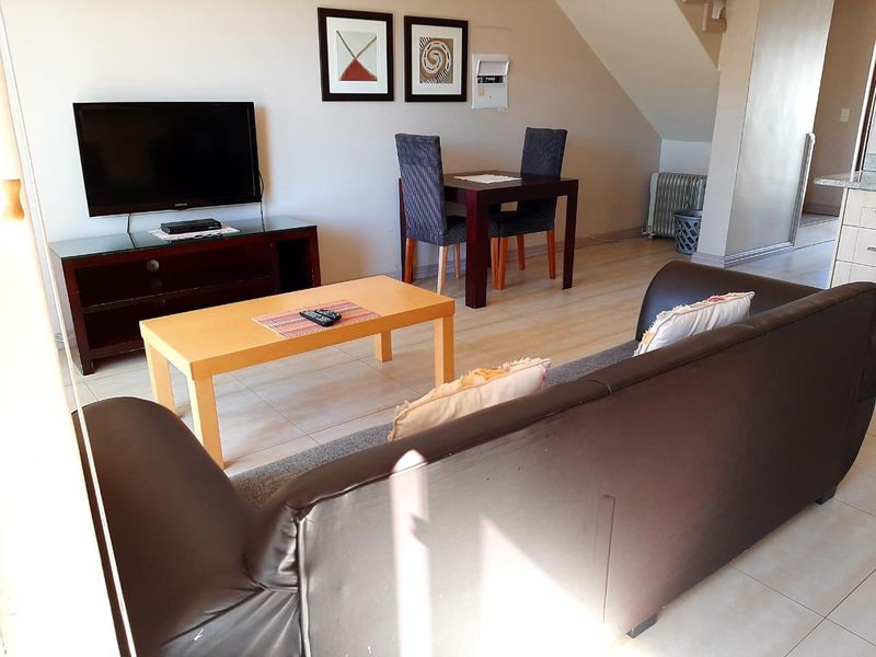 A living room area featuring tiled flooring and an integrated staircase, providing a functional open-plan layout for the apartment.