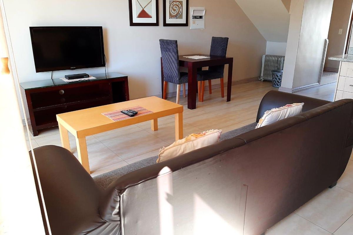 A living room area featuring tiled flooring and an integrated staircase, providing a functional open-plan layout for the apartment.