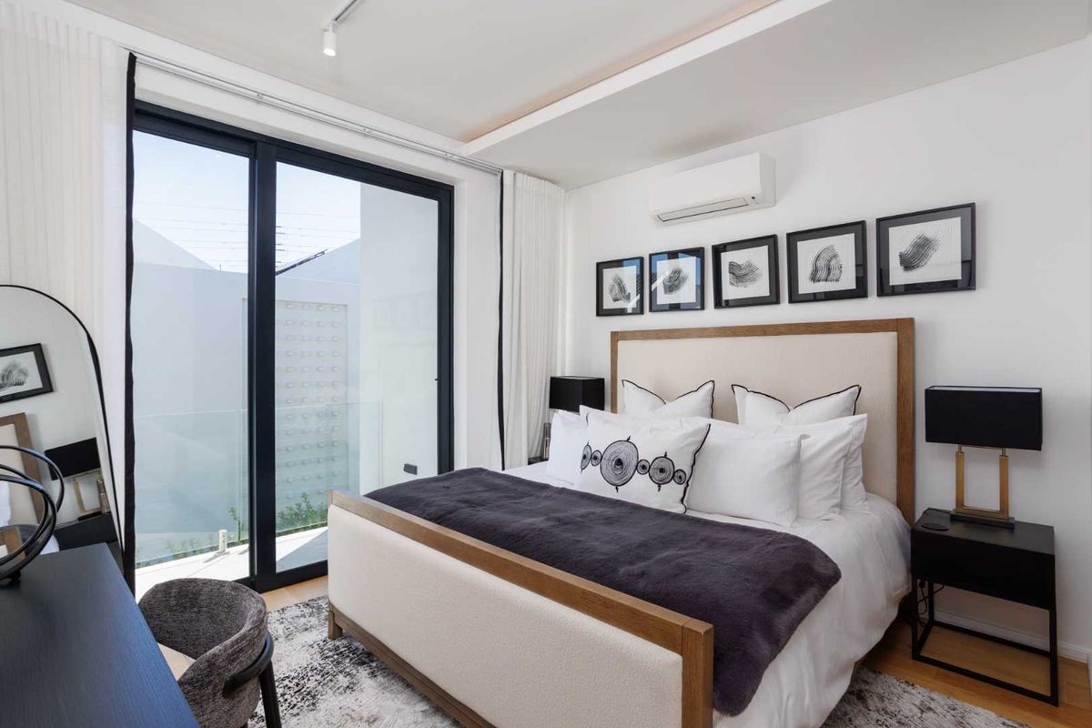 A modern, well-lit bedroom featuring large sliding glass doors leading to a balcony, integrated air conditioning, and high-quality finishes.