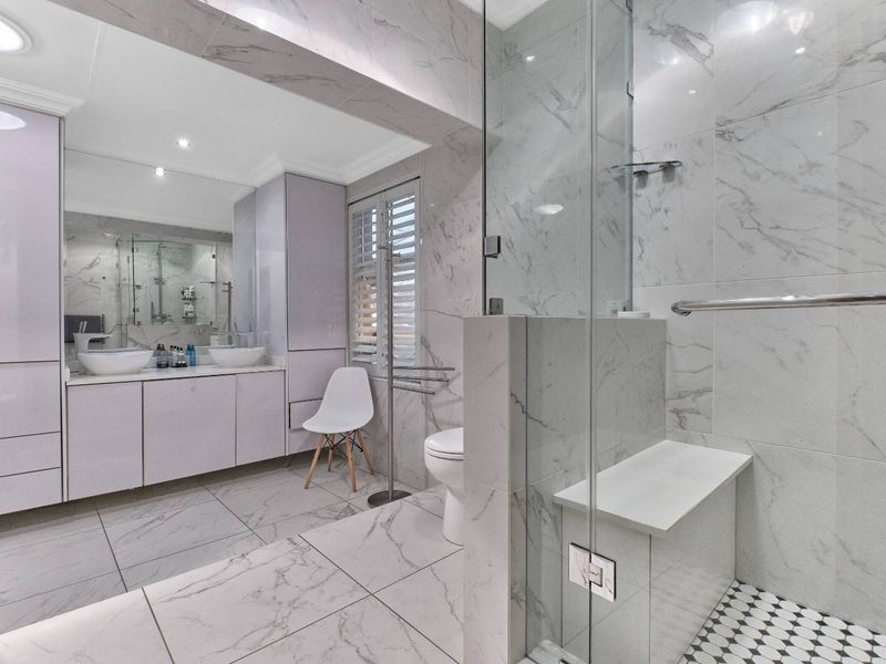 Modern bathroom featuring a double vanity with vessel sinks, large wall mirror, and a spacious walk-in shower with a built-in bench and marble-look tiling.