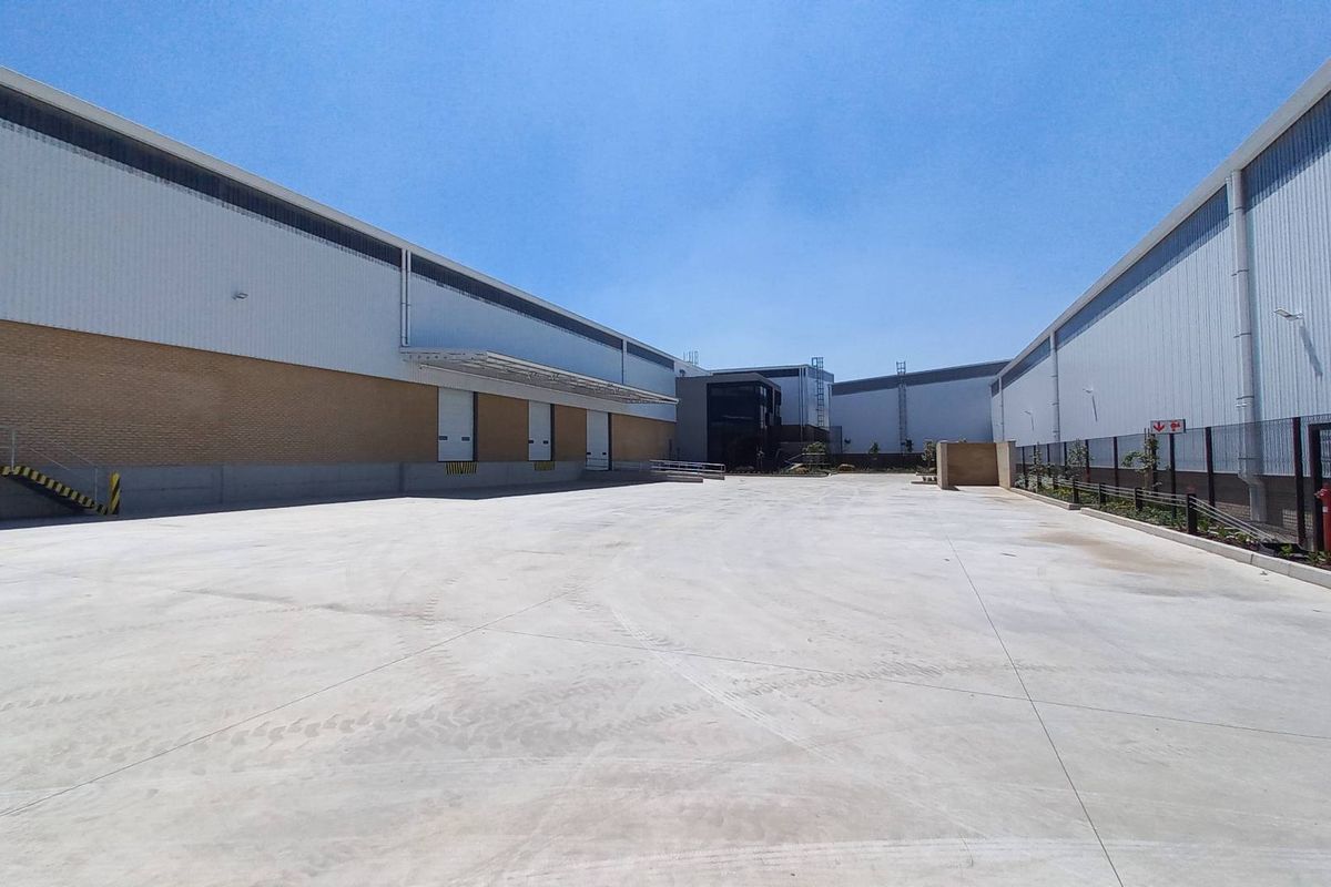 Spacious industrial concrete yard featuring multiple loading docks, metal clad warehouse walls, and secure perimeter fencing, ideal for logistics and heavy vehicle access.