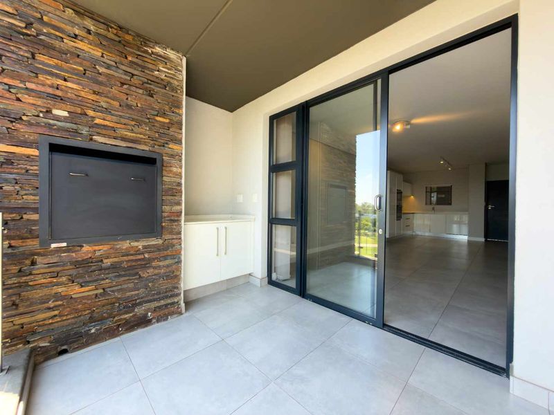 Covered balcony featuring a built-in braai with stone cladding, tiled flooring, and sliding glass doors providing access to the open-plan interior living area.
